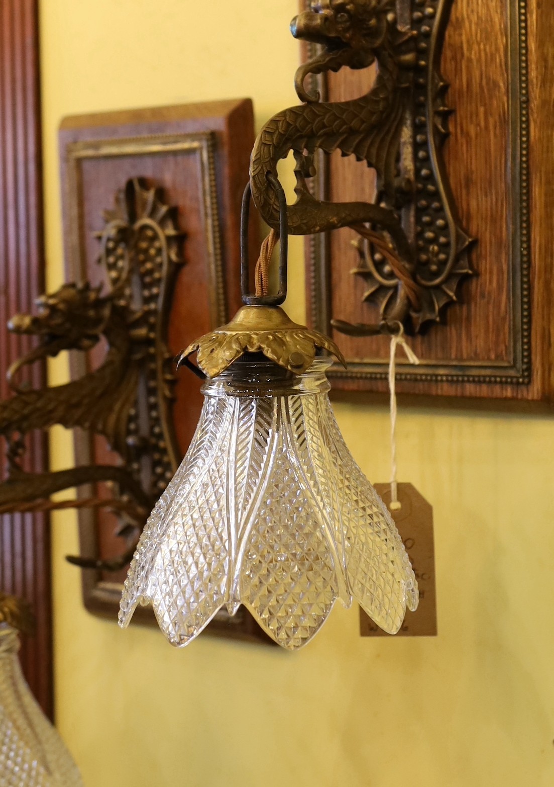 A pair of early 20th century English bronze metal dragon pendant wall lights, with moulded glass shades and mahogany back plates, height overall 35cm
